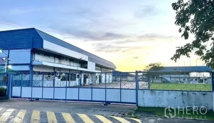 Factory for rent in Bang Bua Thong, Nonthaburi - Entrance gate view to factory complex and landscaped grounds at dusk.
