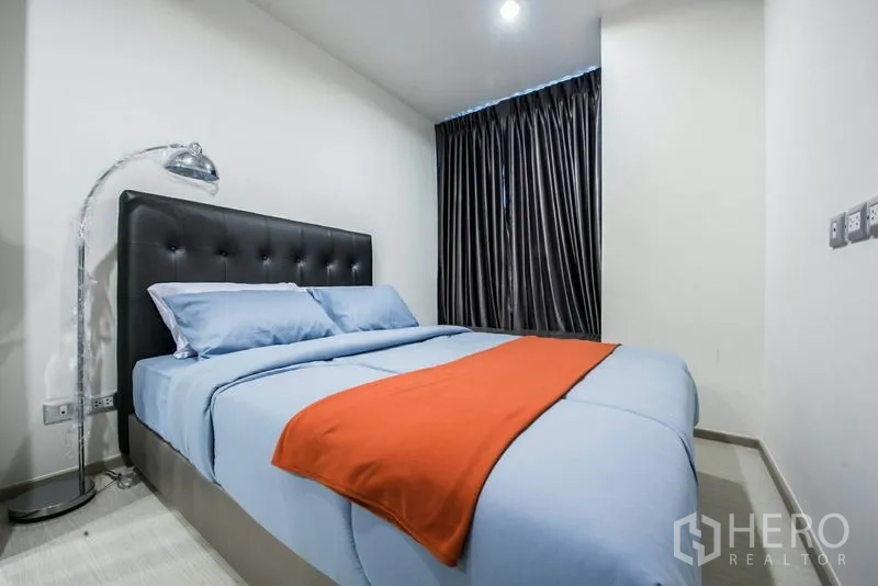 Condominium for rent in Khlong Toei, Bangkok - Cozy bedroom with tufted headboard, blue bedding and dark blackout drapes.