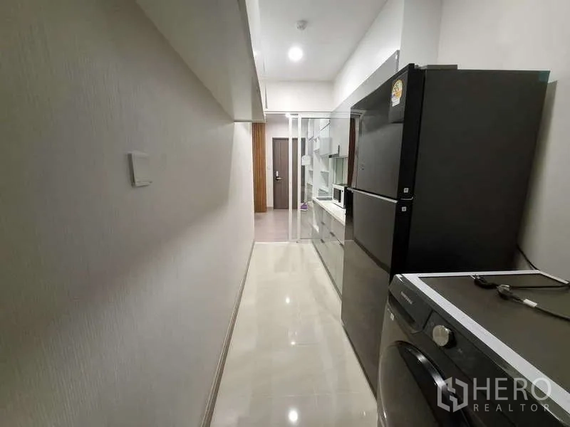 Condominium for rent - Long kitchen corridor with refrigerator and washing machine facing the entry door.