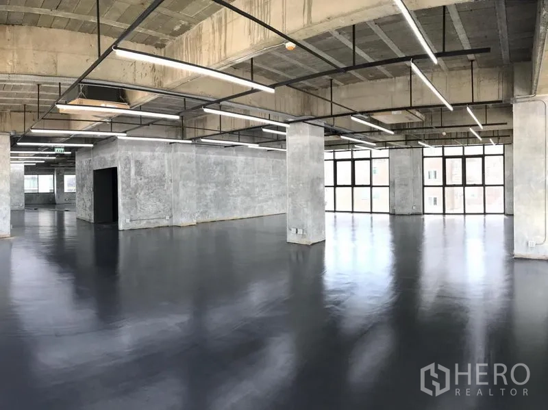 办公空间 出租在Khlong Toei, Bangkok - 宽敞工业风办公区，混凝土立柱与网格天花，环绕窗户引入充足自然光。
