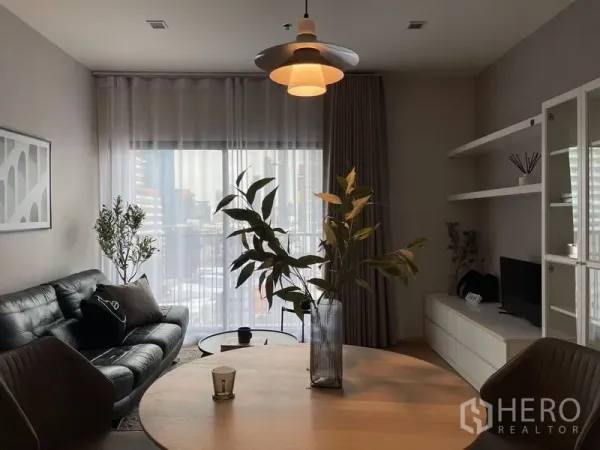 公寓 出租在Watthana, Bangkok - 餐桌与吊灯近景，可见沙发和带纱帘的阳台。