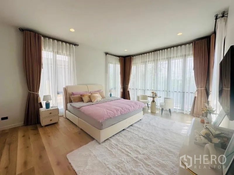 Detached House for rent or sale in Bang Kapi, Bangkok - Primary bedroom with corner windows, upholstered bed, seating nook and plush white rug.