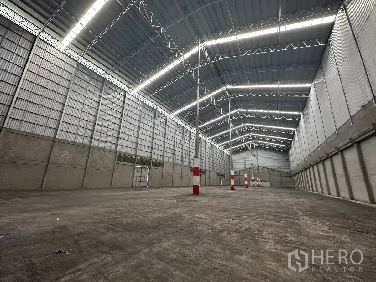 Warehouse for rent in Mueang Pathum Thani, Pathum Thani - Spacious high‑ceiling warehouse interior with steel truss roof, skylight strips and open floor area.