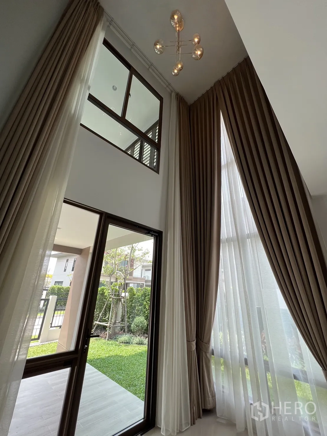 Detached House for rent in Bang Kapi, Bangkok - Double-height living room windows and door opening to a green lawn.