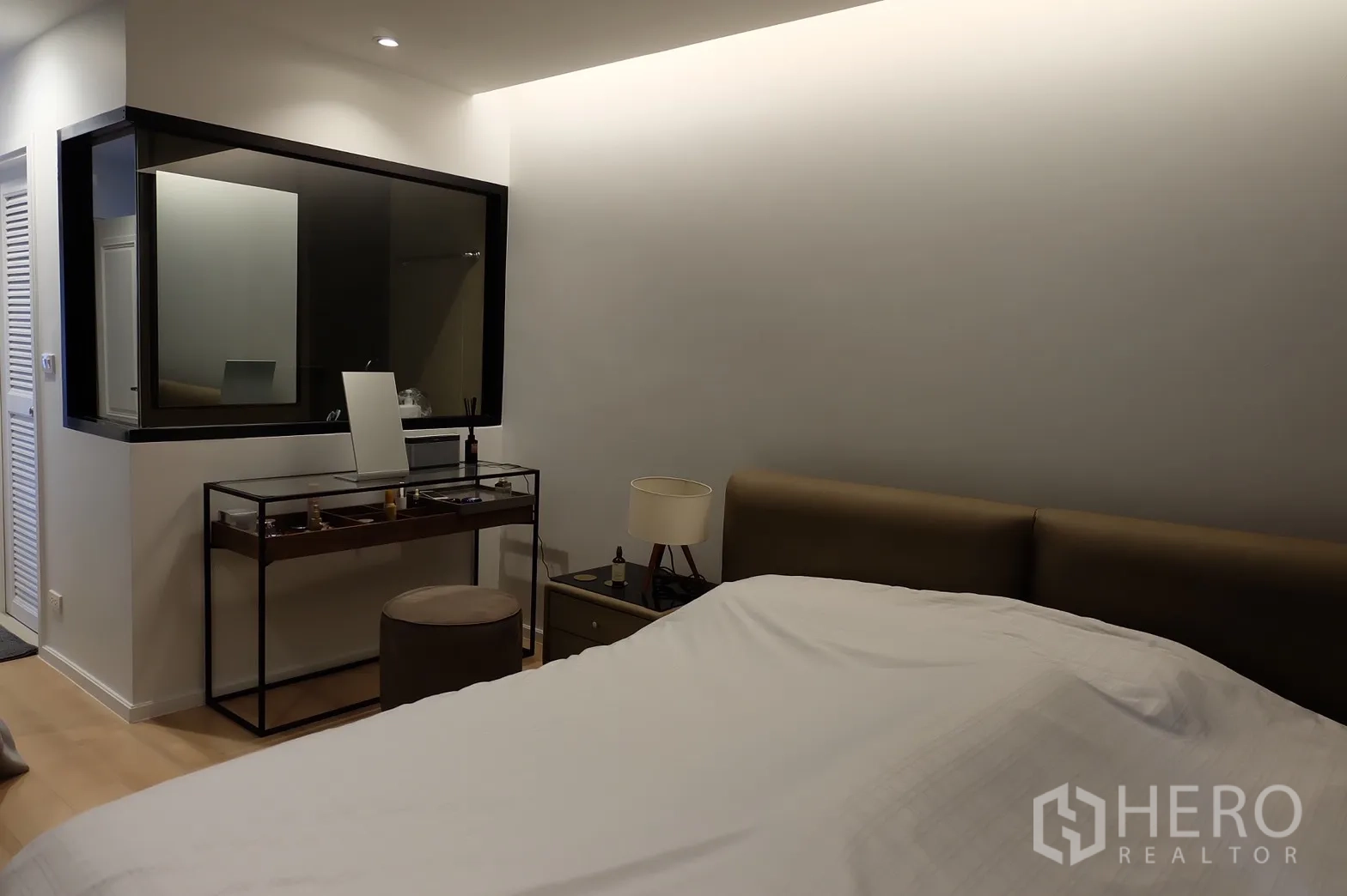 Condominium for rent in Bang Rak, Bangkok - Primary bedroom with dressing table and window to bathroom, featuring soft cove lighting.