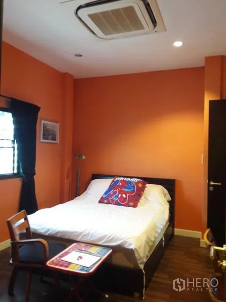 Townhouse for rent or sale in Chatuchak, Bangkok - Cozy bedroom with orange feature wall, bed and ceiling cassette air conditioner.