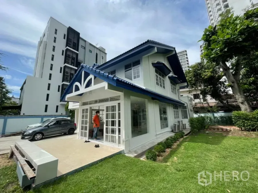 Detached House for rent in Khlong Toei, Bangkok - Two-storey detached house with blue roof, large windows and front terrace beside a green lawn in Khlong Toei.