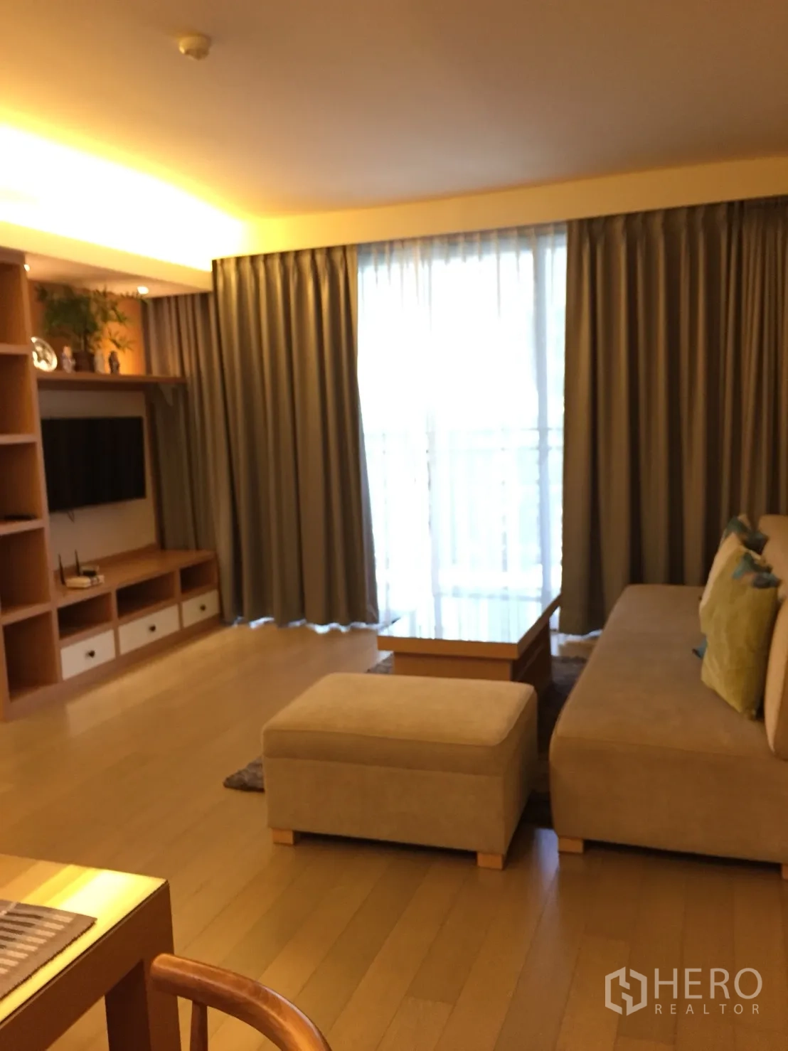 公寓 出租在Watthana, Bangkok - 明亮客厅，沙发与脚凳，内置电视柜及落地窗帘。
