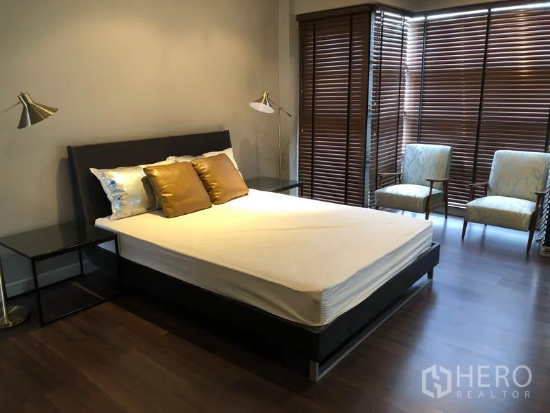 公寓 出租在Watthana, Bangkok - 明亮卧室，木地板、双人床、两张扶手椅，大面积窗配木百叶。