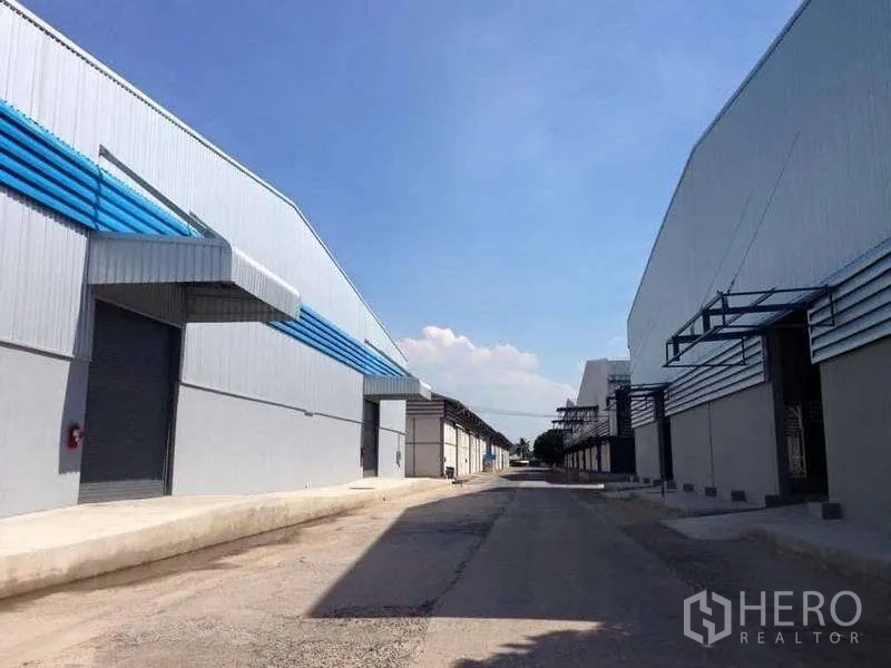 Warehouse for rent in Bang Pa-in, Phra Nakhon Si Ayutthaya - Two warehouse blocks facing a central driveway with multiple roller shutter doors under a blue sky.
