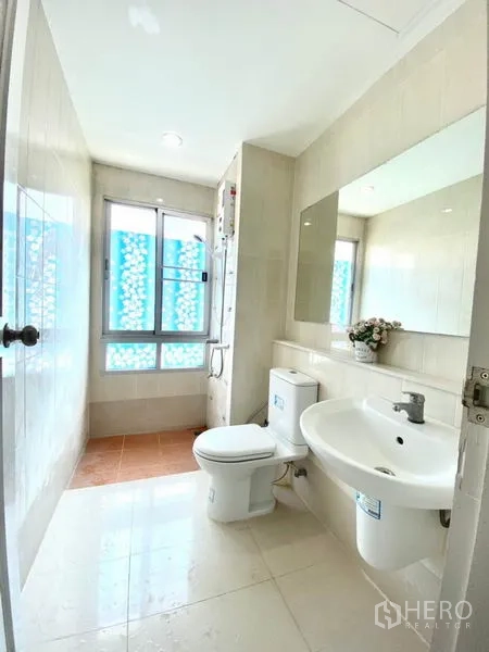 Townhouse for rent in Prawet, Bangkok - Light tiled bathroom with window, vanity, toilet and shower water heater.