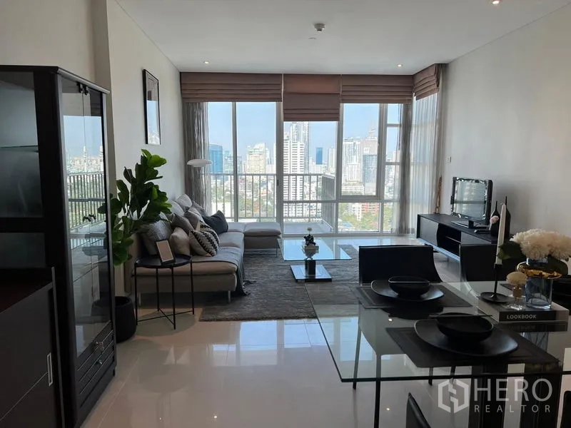 Condominium for rent in Watthana, Bangkok - Living room with panoramic windows, L-shaped sofa, coffee table, and expansive skyline view.