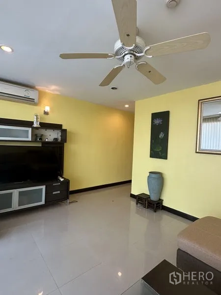 公寓 出售在Watthana, Bangkok - 明亮客厅，设电视柜、黄色特色墙与吊扇。