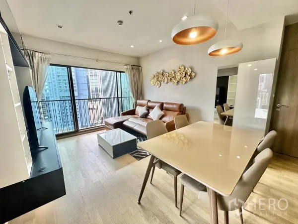 公寓 出租在Bangkok - 明亮的客餐厅，皮沙发、吊灯、电视柜，落地窗连通阳台俯瞰曼谷天际线。