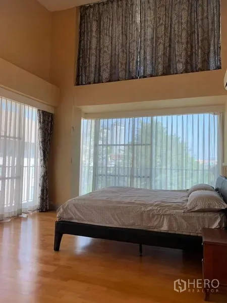 Condominium for sale in Khlong San, Bangkok - Bright master bedroom with tall corner windows, sheer curtains and warm wood flooring.
