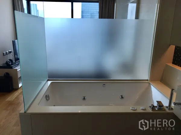 Condominium for rent or sale in Bang Rak, Bangkok - Large soaking bathtub with frosted glass divider in a modern bathroom.