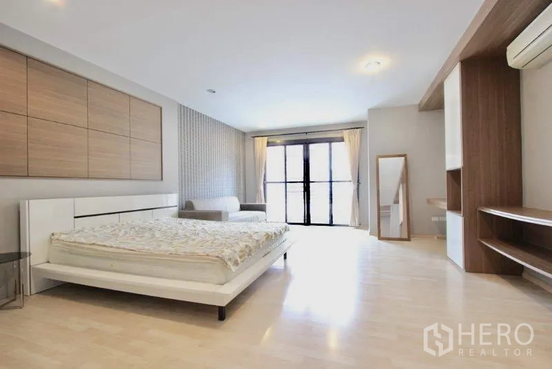 Townhouse for sale in Suan Luang, Bangkok - Large master bedroom with built-in storage, seating area, and balcony doors.