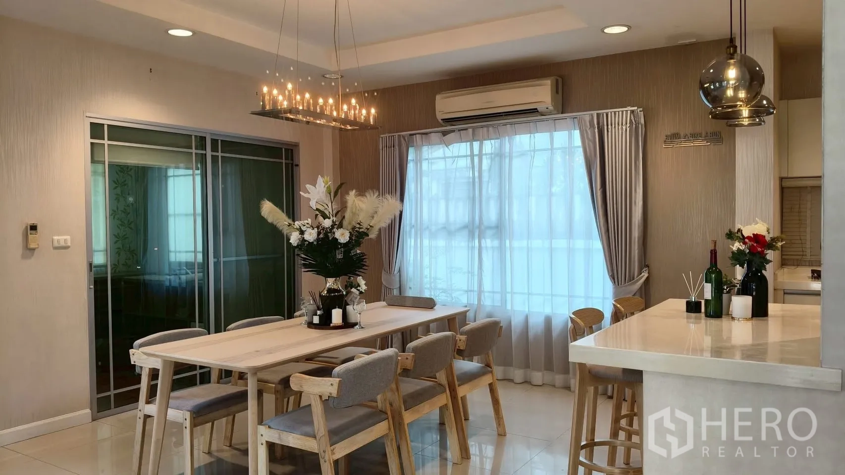独立式住宅 出租或出售在Mueang Samut Prakan, Samut Prakan - 餐区木桌六椅配水晶吊灯，旁连开放式厨房吧台。