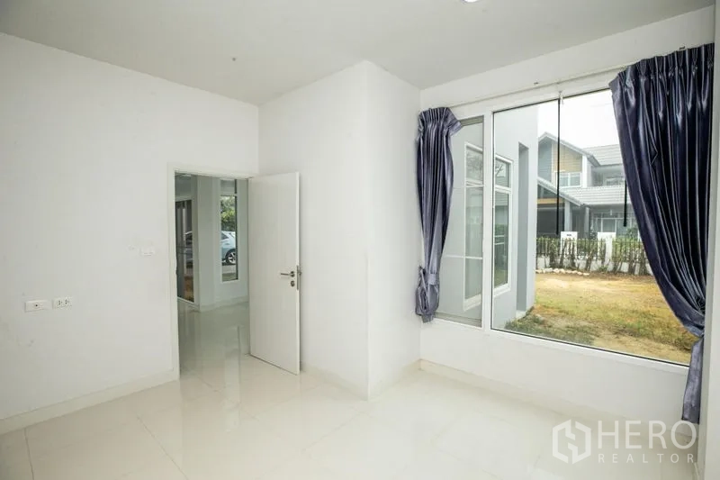 Detached House for rent or sale in Lam Luk Ka, Pathum Thani - Sunlit bedroom with corner windows and wood floors.