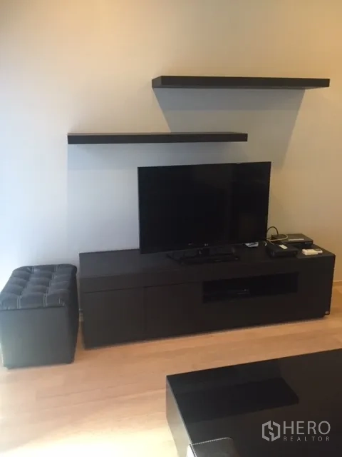Condominium for rent in Bangkok - Media wall featuring a flat-screen TV on a low cabinet with floating shelves and light wood flooring.