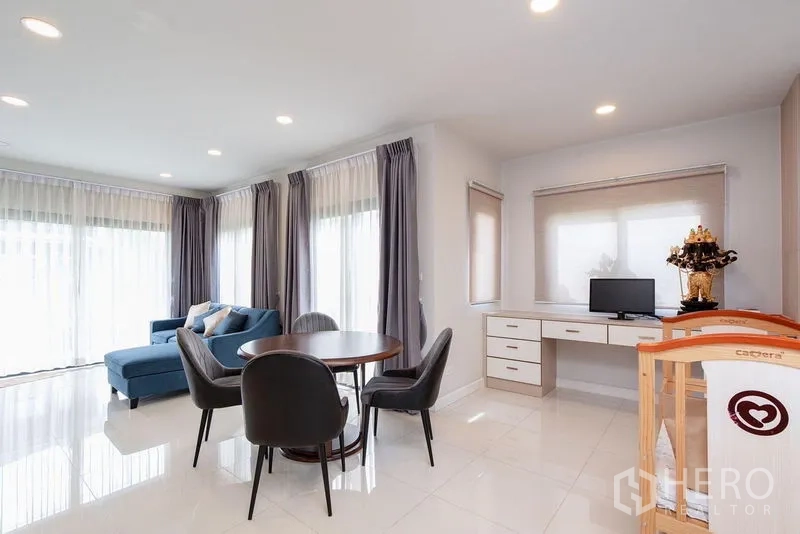บ้าน ให้เช่าในBang Phli, Samut Prakan - มุมนั่งเล่น‑ทานข้าว โซฟาสีฟ้า โต๊ะกลม และโต๊ะทำงาน