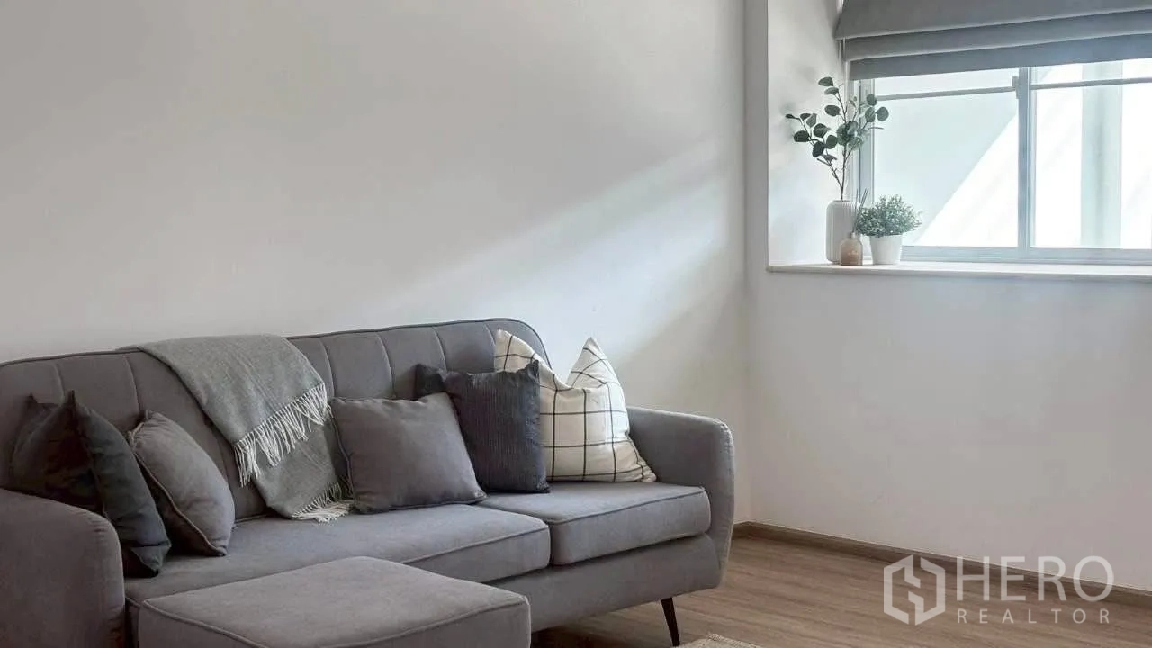 联排别墅 for rent in Prawet, Bangkok - 靠窗灰色沙发近景，靠垫层叠，摆放绿植点缀。