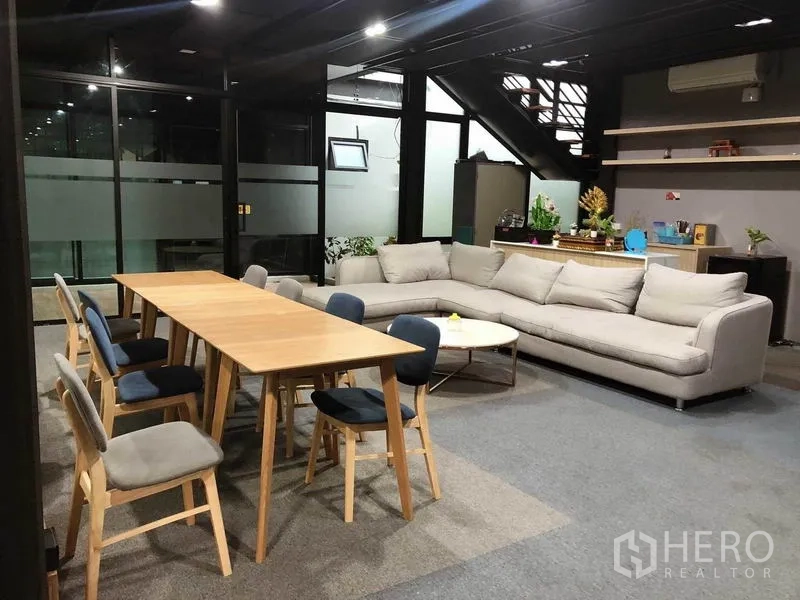 Office Space for rent in Bang Na, Bangkok - Open‑plan office zone with long table, sectional sofa, shelving and staircase.