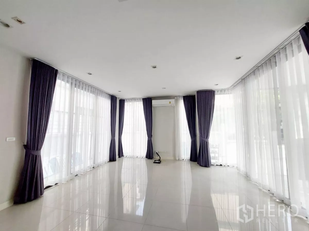 Townhouse for rent in Lat Phrao, Bangkok - Long living room wrapped in floor-to-ceiling windows with purple drapes and polished tile flooring.