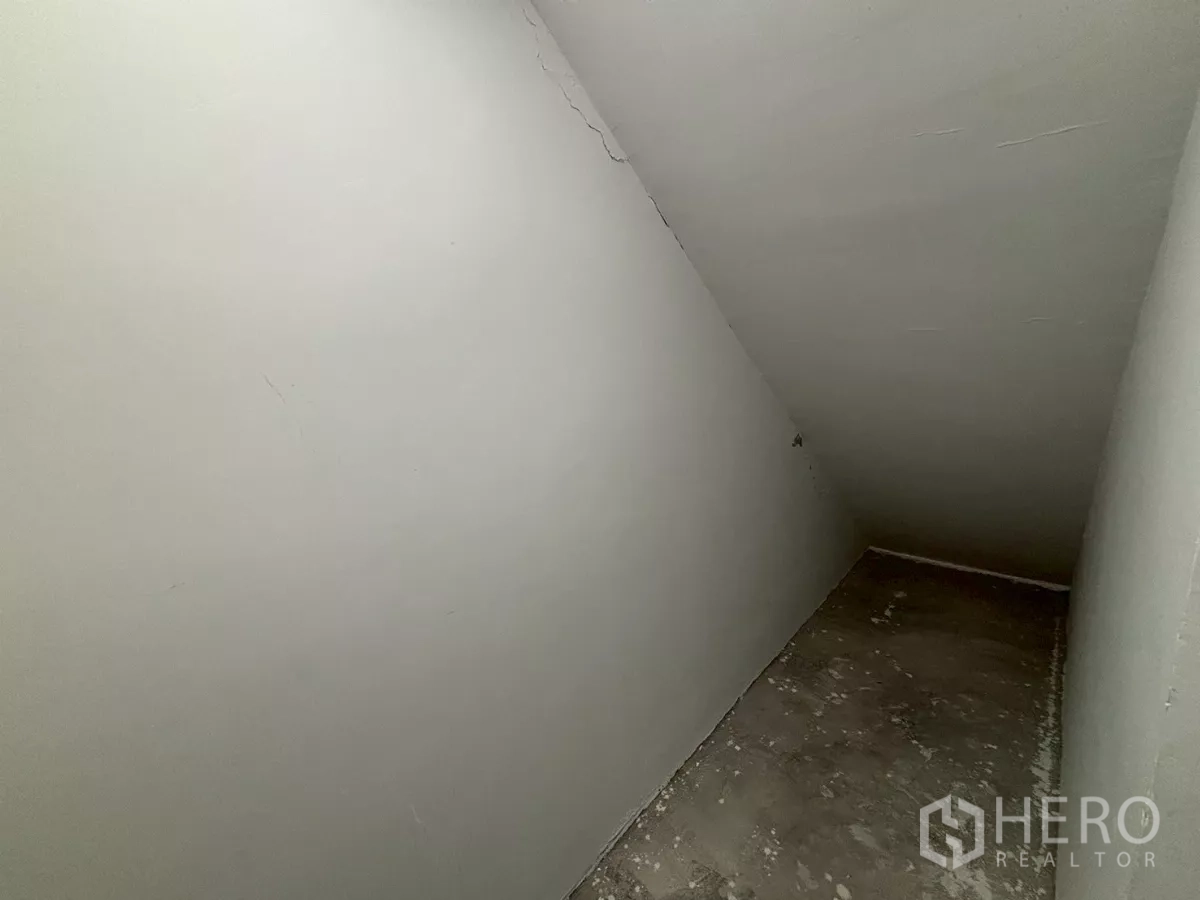 Condominium for sale in Bang Kho Laem, Bangkok - Empty under-stairs storage room with a sloped ceiling and unfinished floor.