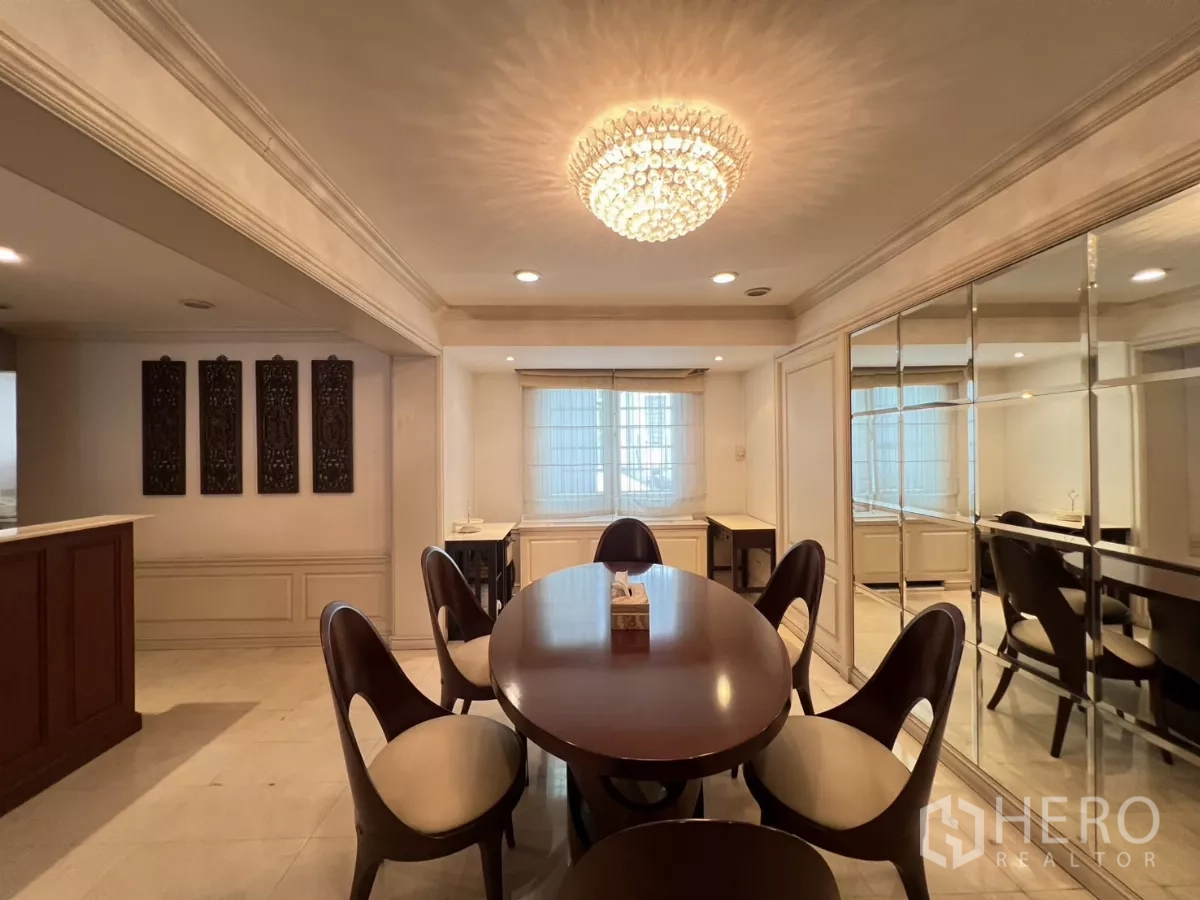 Townhouse for sale in Watthana, Bangkok - Formal dining area with oval table, crystal chandelier and mirrored feature wall.