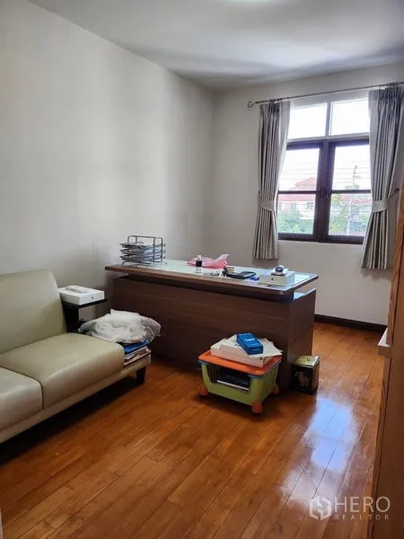 Detached House for rent in Bang Kapi, Bangkok - Bright home office with a desk, sofa and curtained window over wood floors.