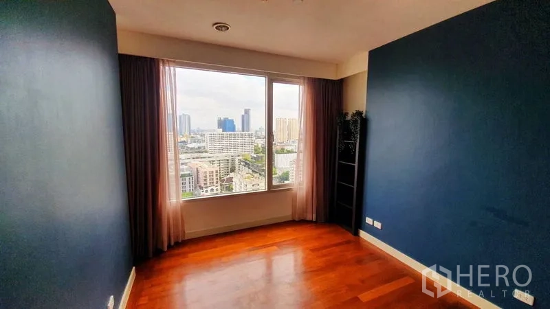 Condominium for rent in Watthana, Bangkok - Bedroom with hardwood floors, deep blue wall and large window facing the Bangkok skyline.