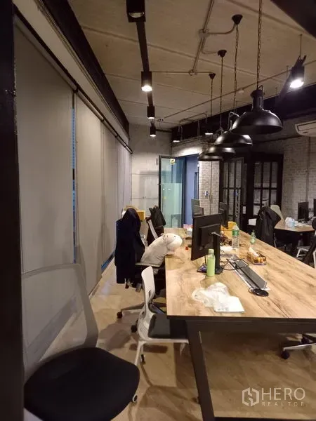 Office Space for rent in Chatuchak, Bangkok - Shared desk area with pendant lights, roller blinds and computer stations along a timber table.