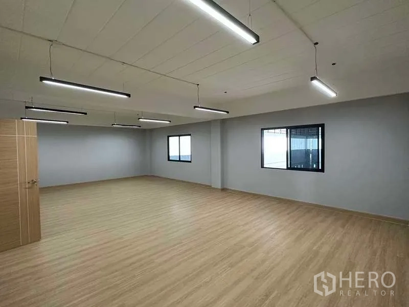 Factory for sale in Khlong Luang, Pathum Thani - Large open-plan office room with wood-look floors, windows and suspended lights.