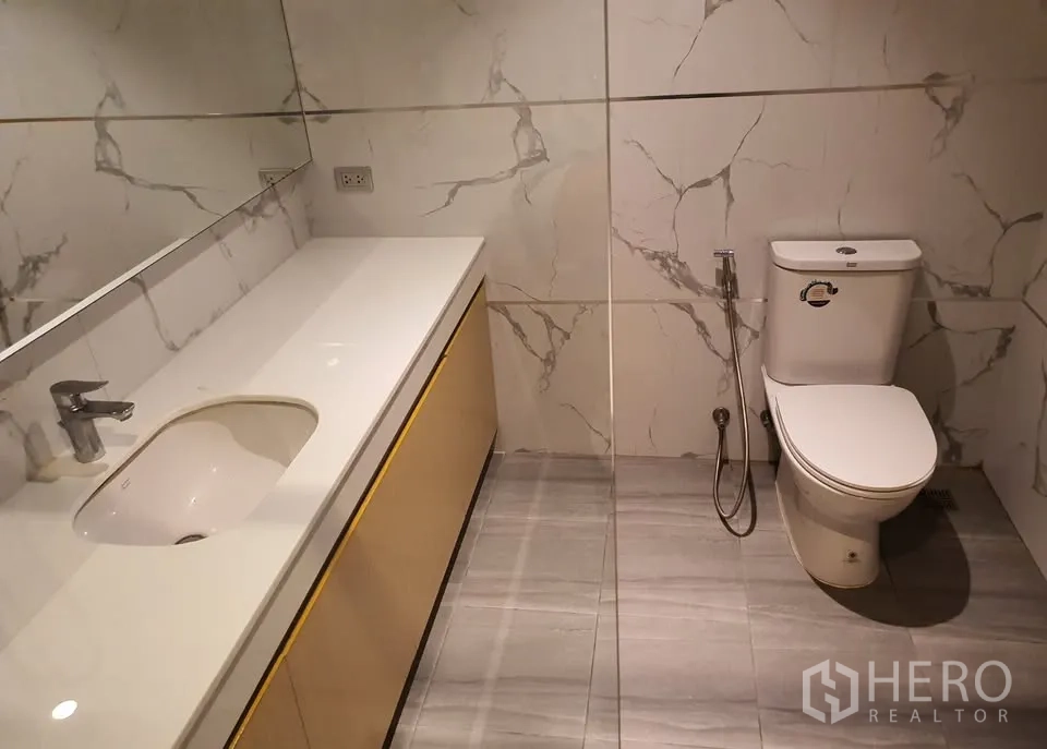 Condominium for rent in Watthana, Bangkok - Guest bathroom with extended countertop vanity, toilet and marble-effect walls.