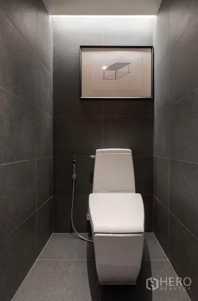 Condominium for rent in Phaya Thai, Bangkok - Compact toilet room with gray tiles, spray hose and framed artwork.
