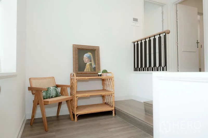 Detached House for rent or sale in Saphan Sung, Bangkok - Upstairs landing nook with rattan chair, shelving and framed artwork.