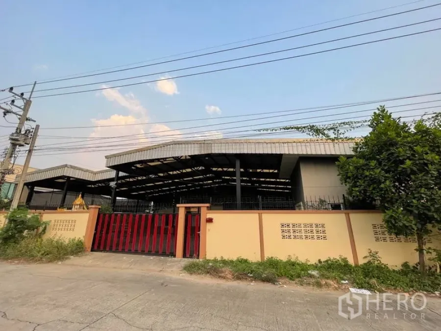 Factory for rent in Lat Lum Kaeo, Pathum Thani - Street-facing facade with a tall perimeter wall and red sliding gate.