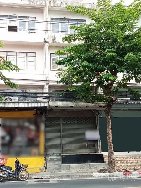 Shophouse for rent in Phra Khanong, Bangkok - Street-front facade of a multi-story shophouse in Phra Khanong with a metal roller shutter and a shade tree.