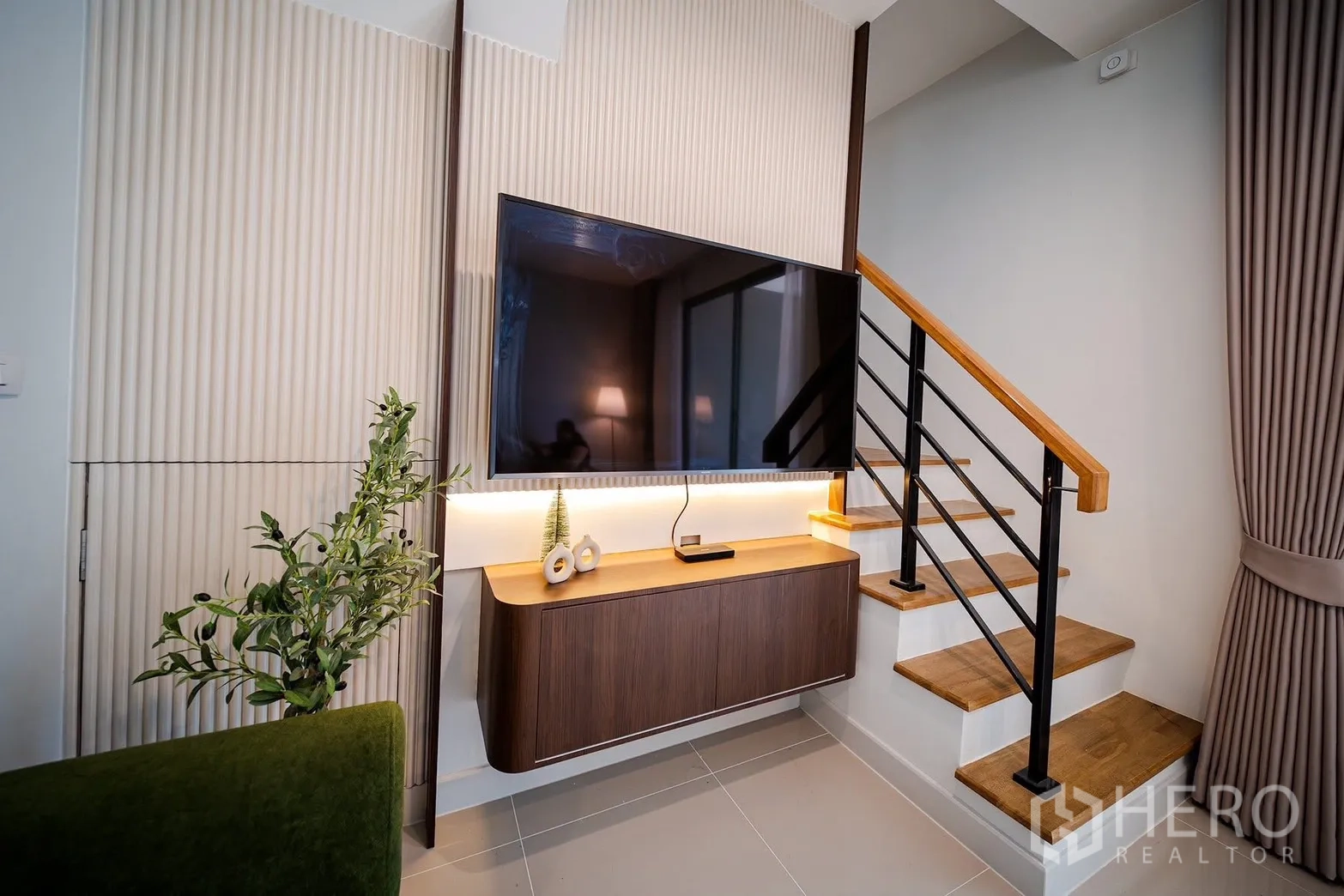 Townhouse for rent in Bang Phli, Samut Prakan - TV feature wall and floating cabinet beside a staircase with wooden treads.