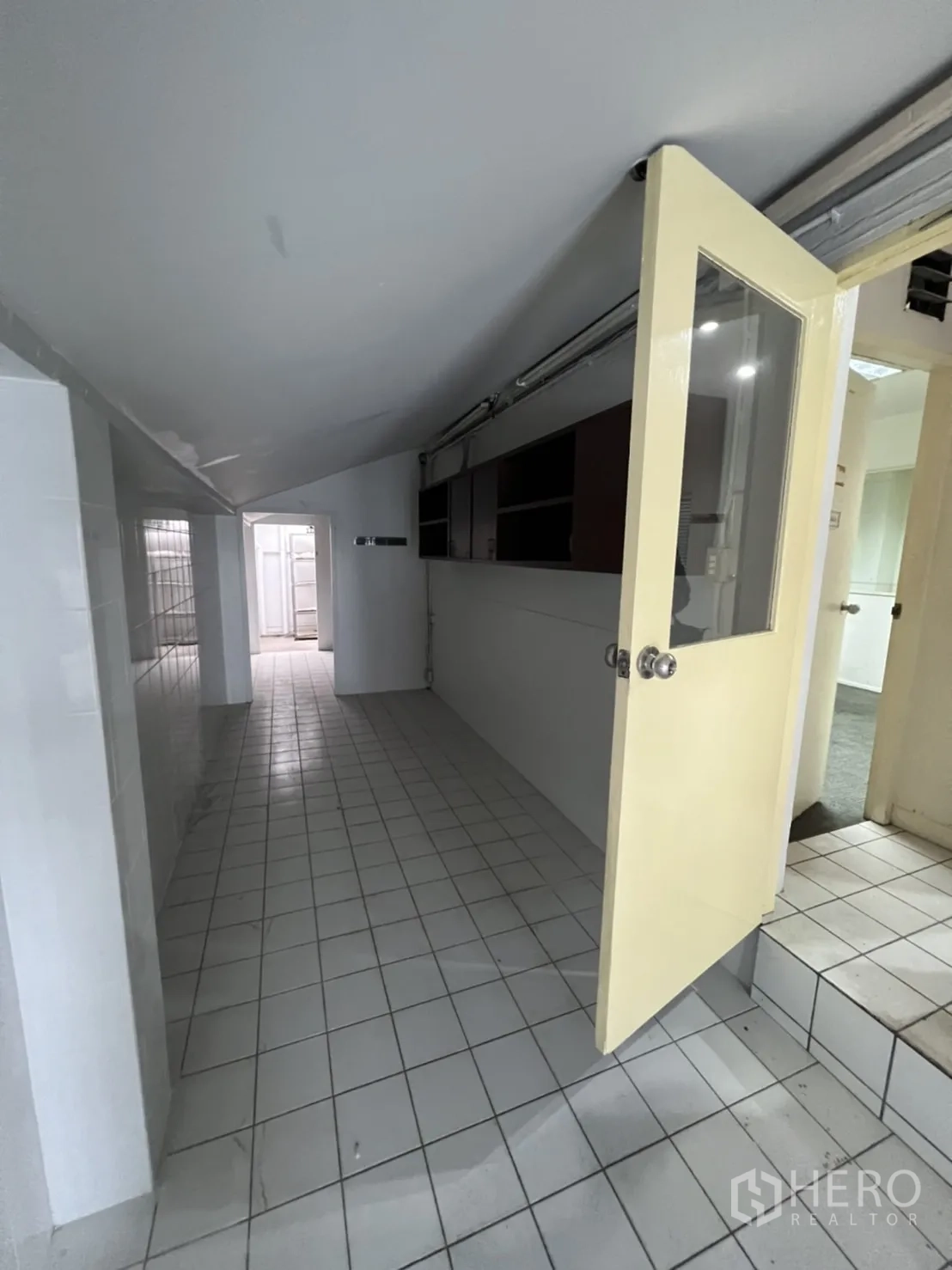 Shophouse for rent or sale in Watthana, Bangkok - Narrow tiled corridor with sloped ceiling and a glass door.
