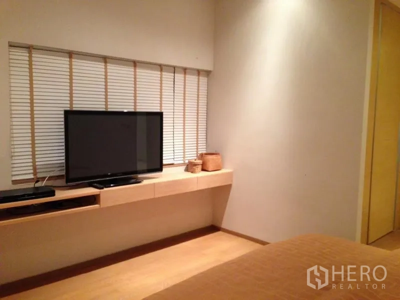 Condominium for sale in Bang Rak, Bangkok - Bedroom media wall with long shelf, flat-screen TV and blinds.