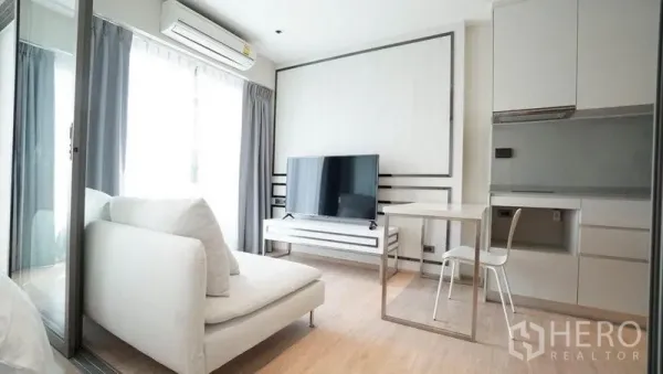 Condominium for sale in Khlong Toei, Bangkok - Light-filled living room with white sofa, large TV, dining table for two and compact kitchenette.