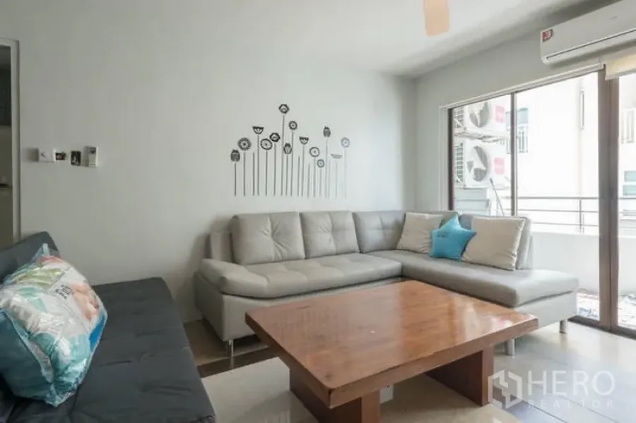 公寓 出租在Watthana, Bangkok - 转角客厅，L型沙发、木质茶几、空调，并可直达阳台。