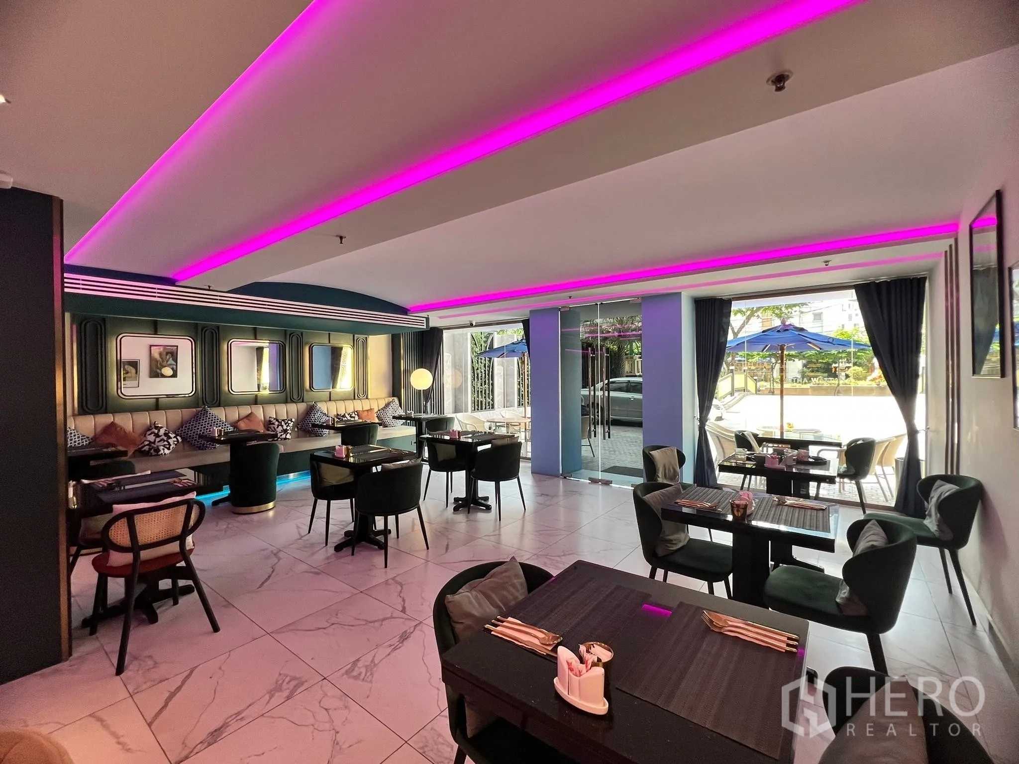 Retail Space for rent - Bright dining area with glass entrance, outdoor patio umbrellas and modern tables under pink light strips.