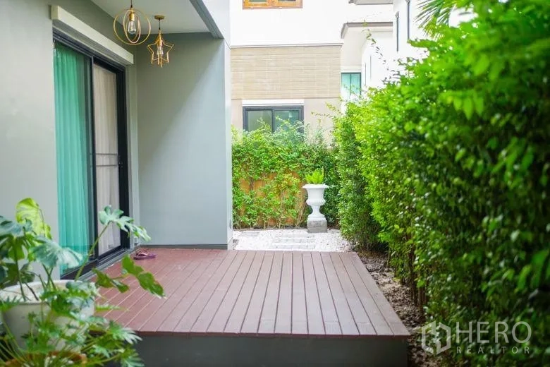 Detached House for rent in Sai Mai, Bangkok - Shaded wooden patio beside sliding glass doors and a green hedge at a detached house in Sai Mai.