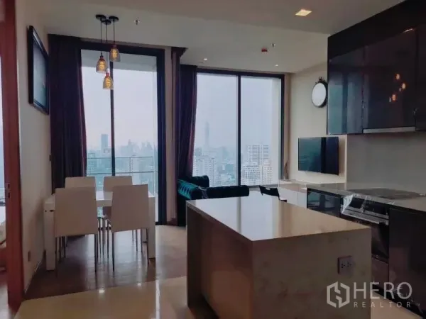 Condominium for rent or sale in Watthana, Bangkok - Modern kitchen island and dining area facing a balcony, with panoramic skyline through glass walls.