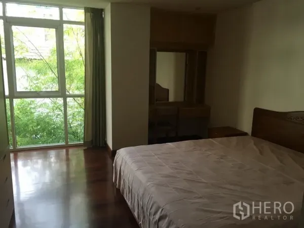 公寓 出租或出售在Watthana, Bangkok - 主卧室带落地窗望向绿景，木地板与梳妆台。