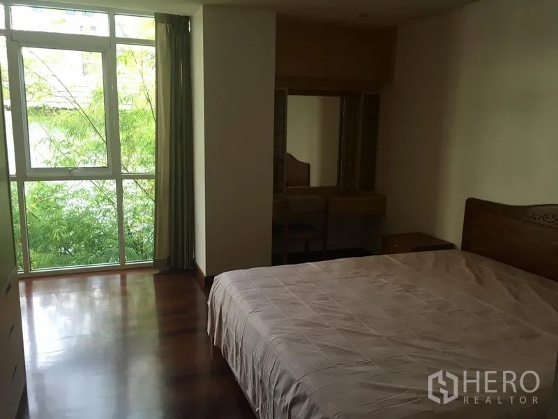 公寓 出租或出售在Watthana, Bangkok - 主卧室带落地窗望向绿景，木地板与梳妆台。