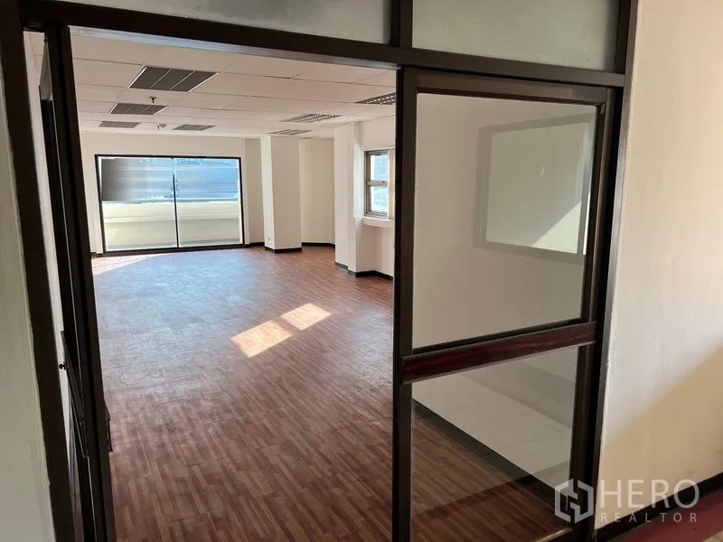 办公空间 出租在Pathum Wan, Bangkok - 从玻璃入口望向宽敞办公区，自然采光充足，木纹地板质感温暖。